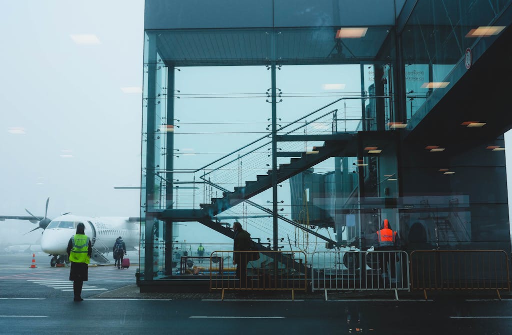 Passengers boarding an airplane at Riga Airport amidst fog, showcasing modern airport architecture.